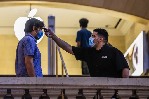 Сотрудник магазина Apple на Центральном вокзале Нью-Йорка измеряет температуру посетителя, 2020 год